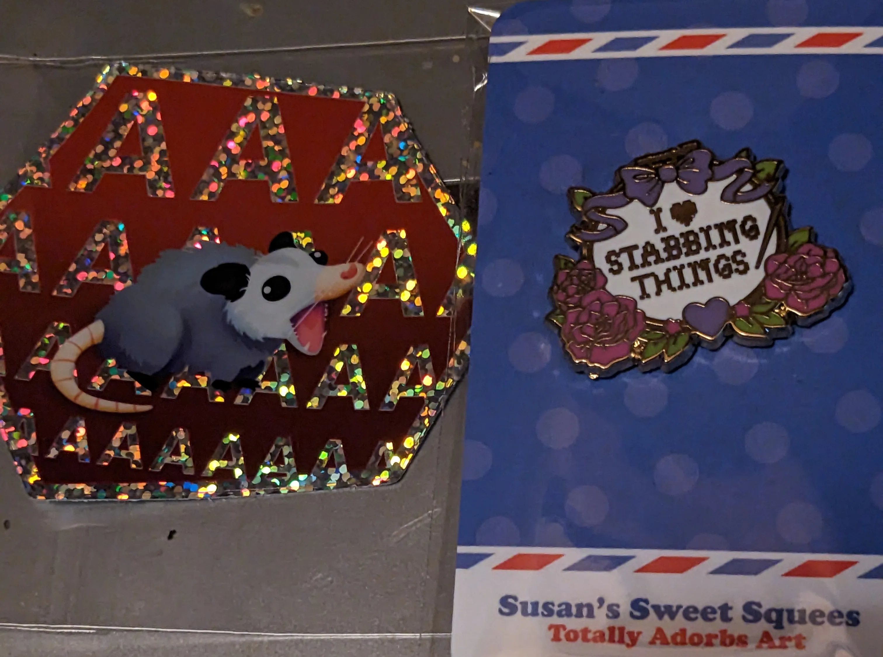 Image a sticker of a possum screaming and an enamel pin that says I heart stabbing things