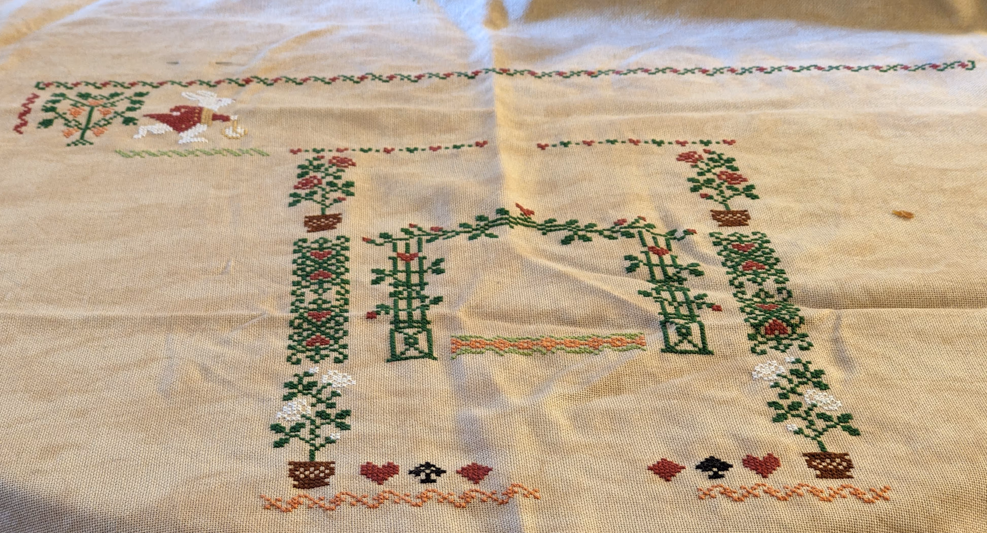 A large cross stitch featuring the white rabbit from Alice in Wonderland with several borders of roses and suits.