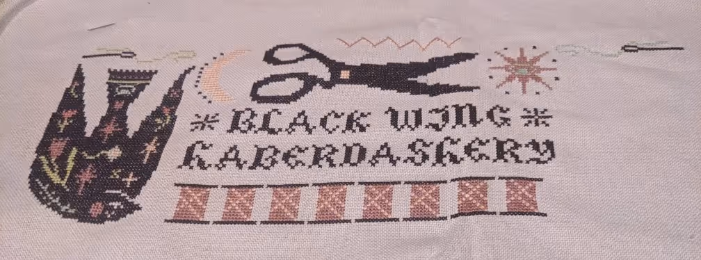 Words read as Black Wing Haberdashery surrounded by sppols of thread, threaded needles, sun, moon, and a bird