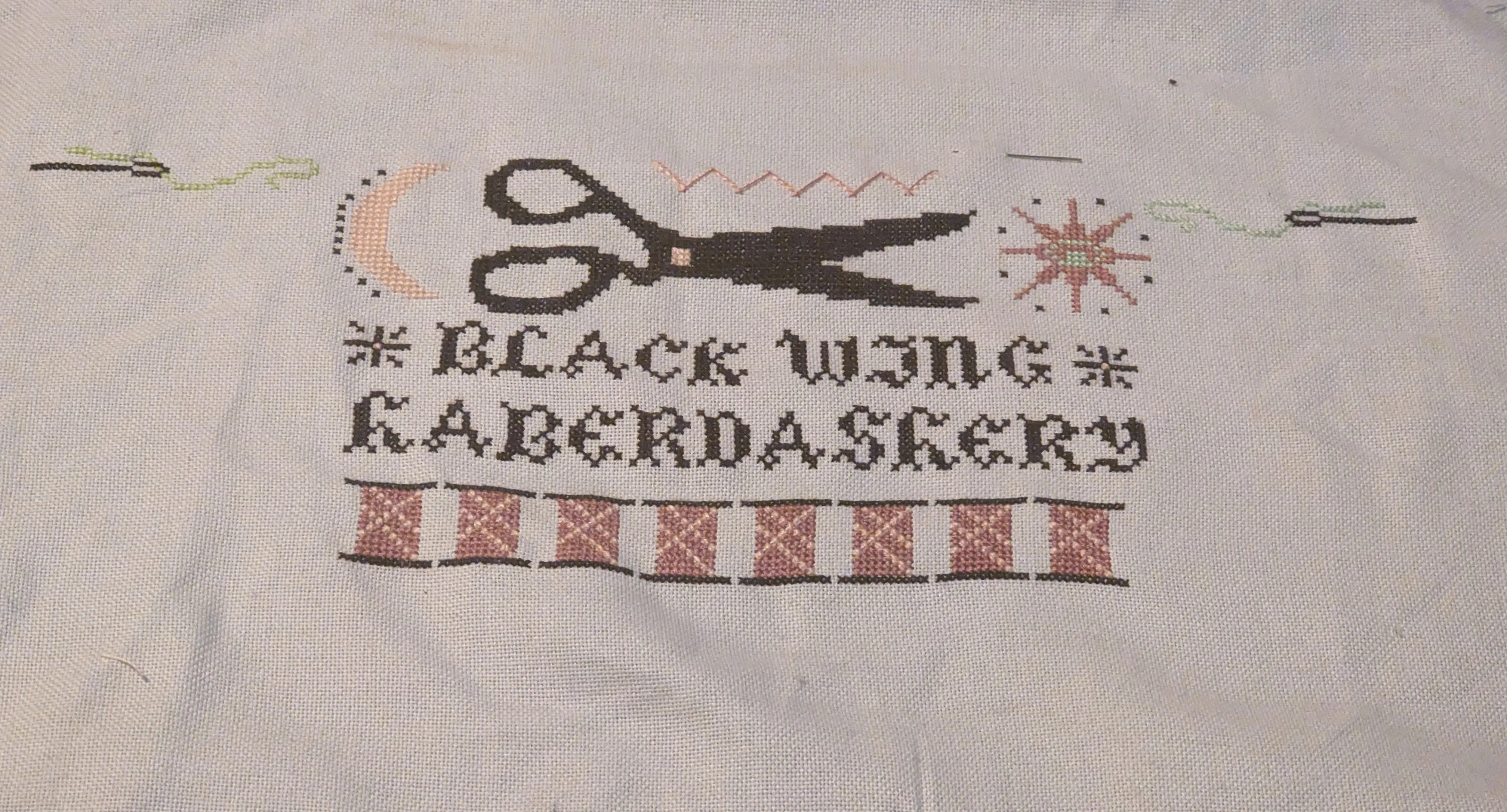 A cross stitch of a sign, spools of thread, sun, moon, needles, and scissors