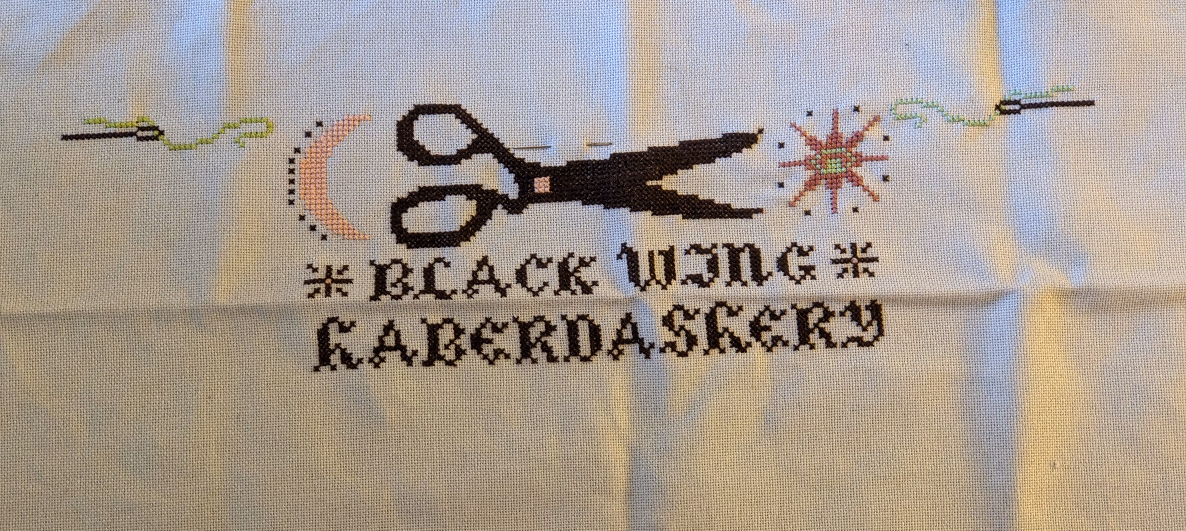 Image of a text that reads black wing haberdashery with blackbirds, thread, needles, and scissors