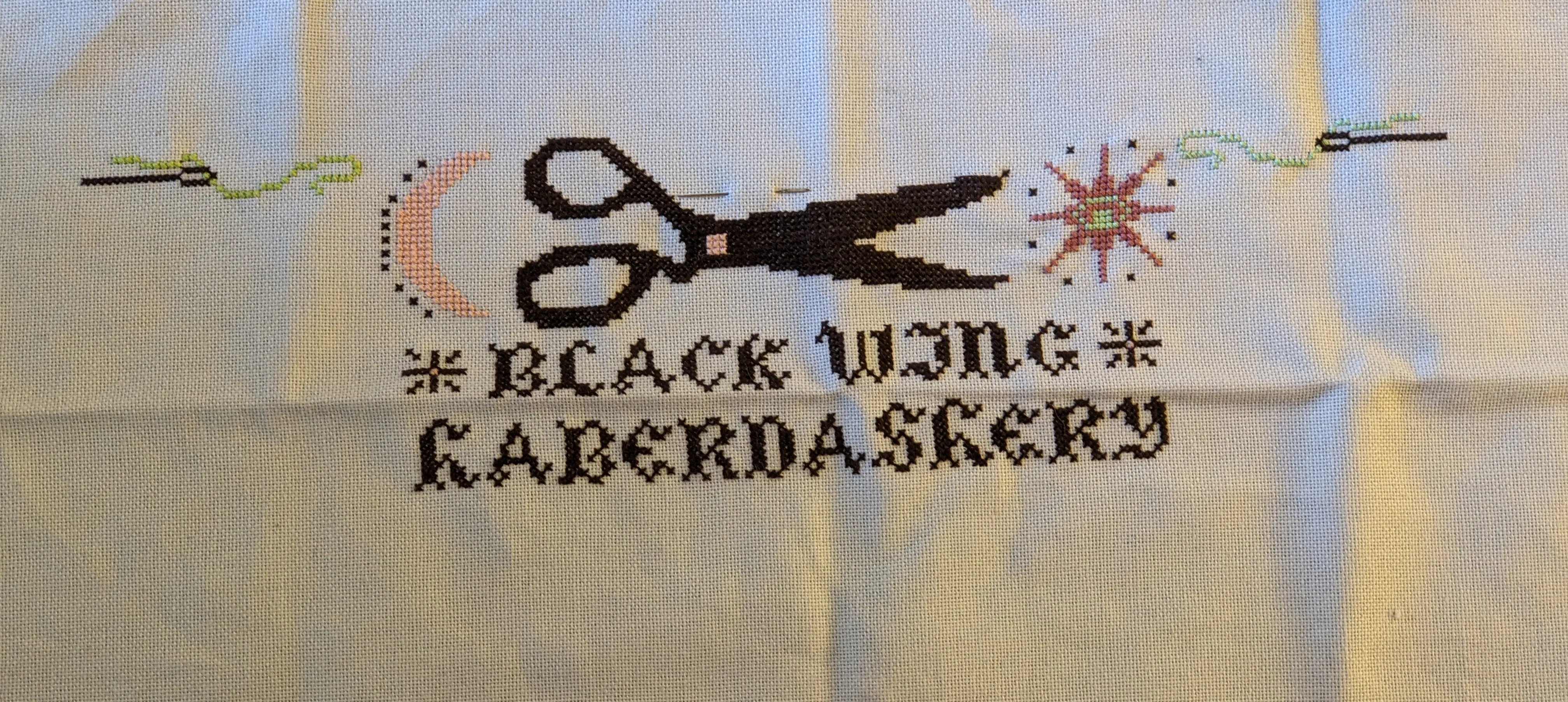 Image of embroidery thread spools, needle and thread, a sun and moon, and birds in cross stitch