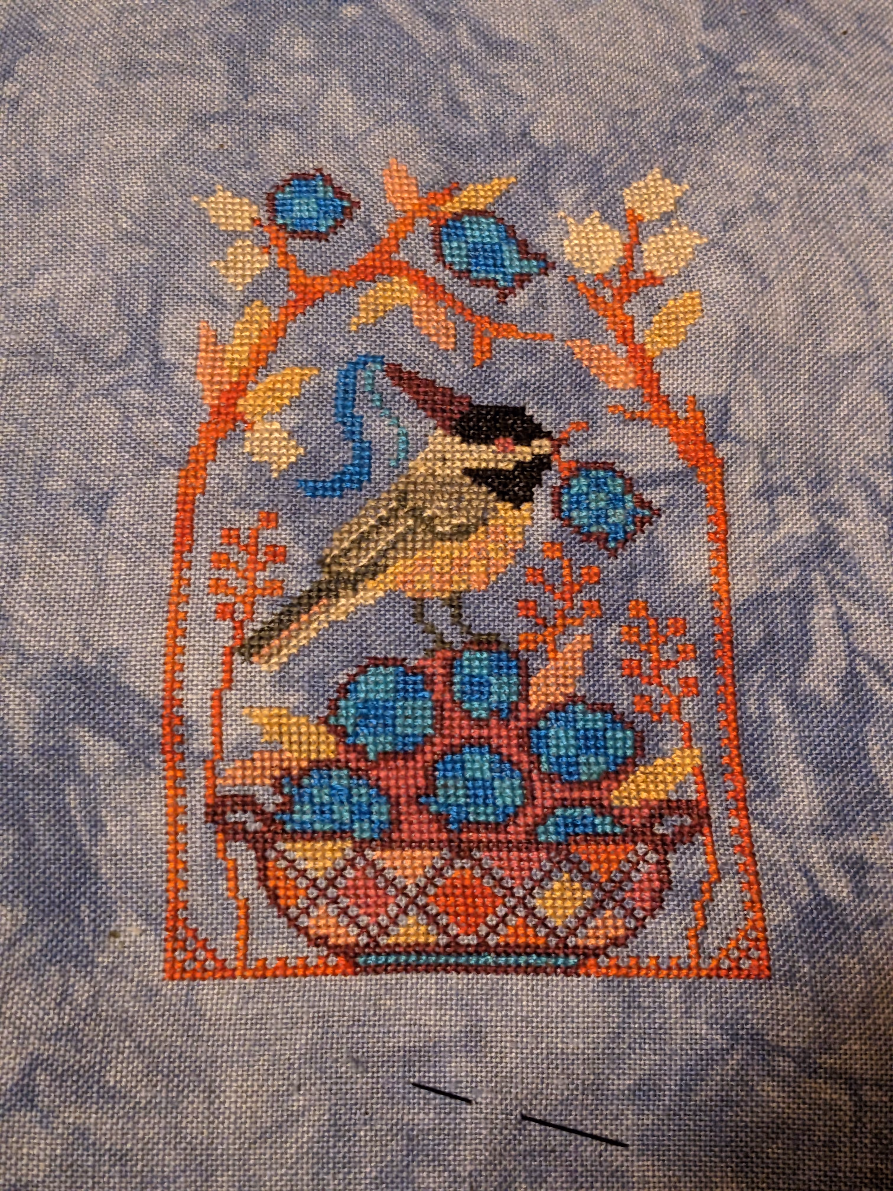 A chickadee holds a blueberry in its mough while sitting a top a basket of blueberries surrounded by branches .