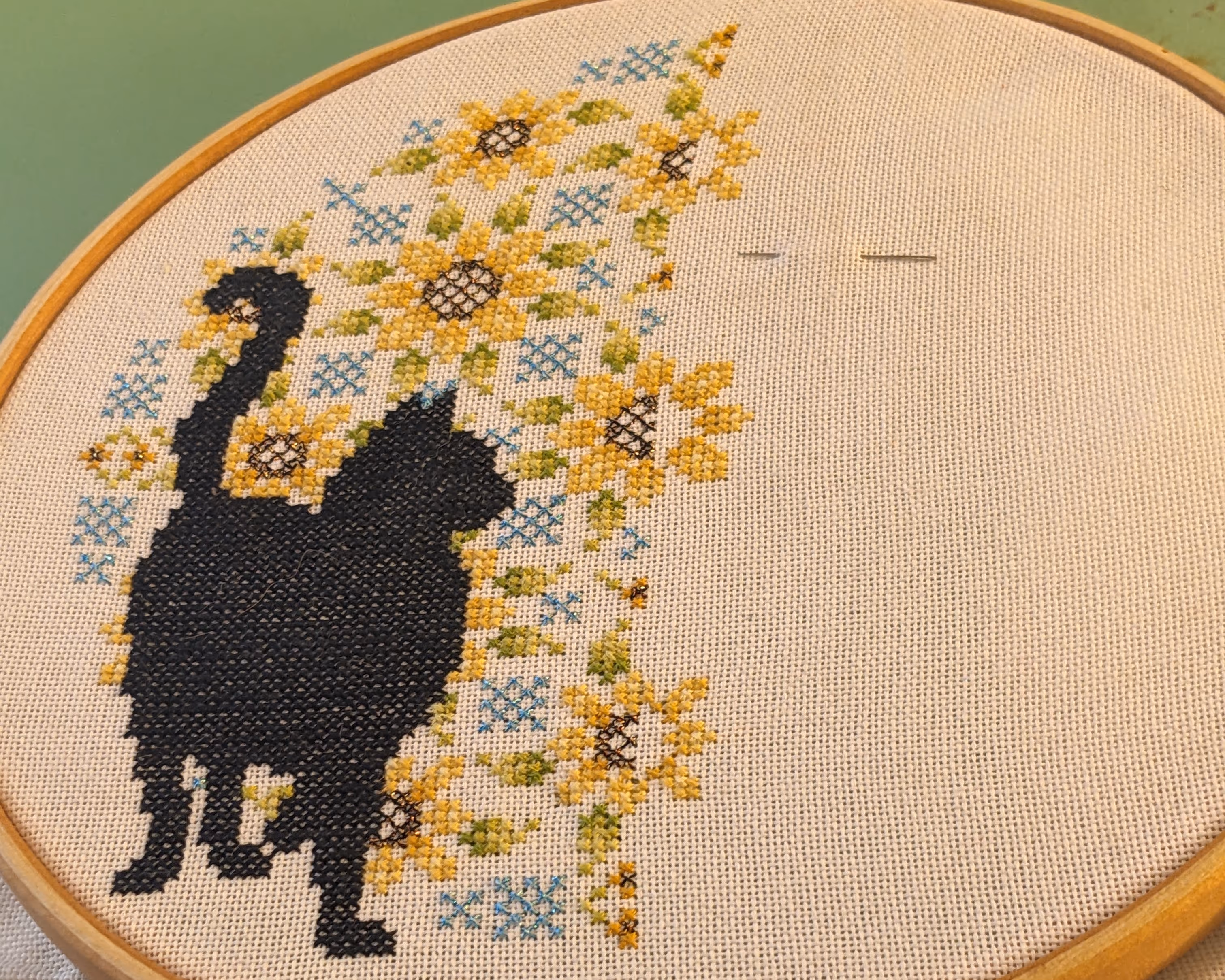 Image of a black cat inside of a mandala with sunflowers cross stitch in a wooden embroidery hoop