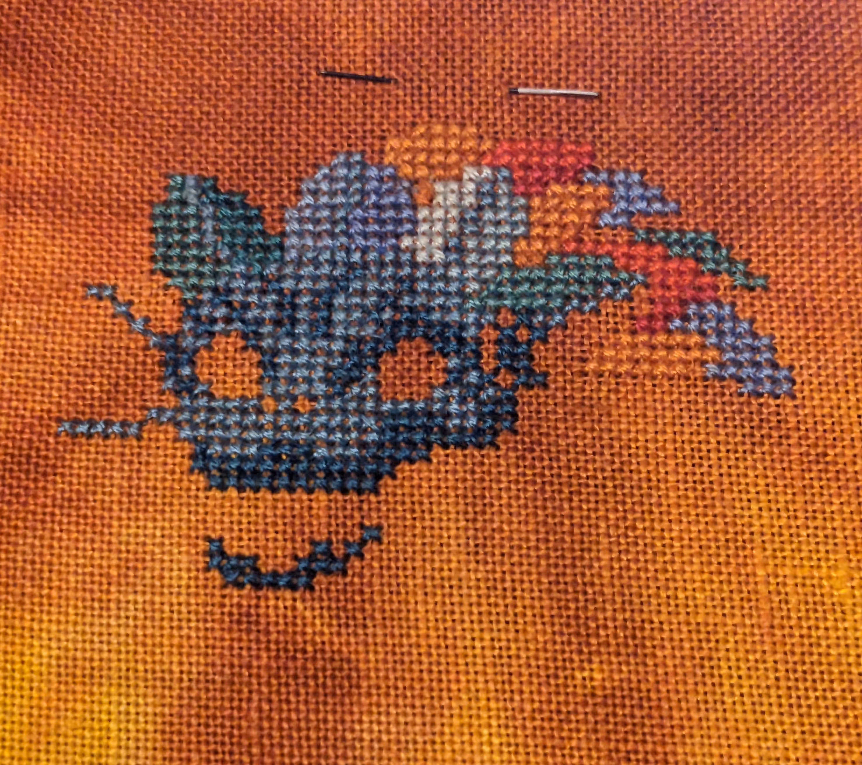A Cross stitch of a dragon with a blue body and orange mane
