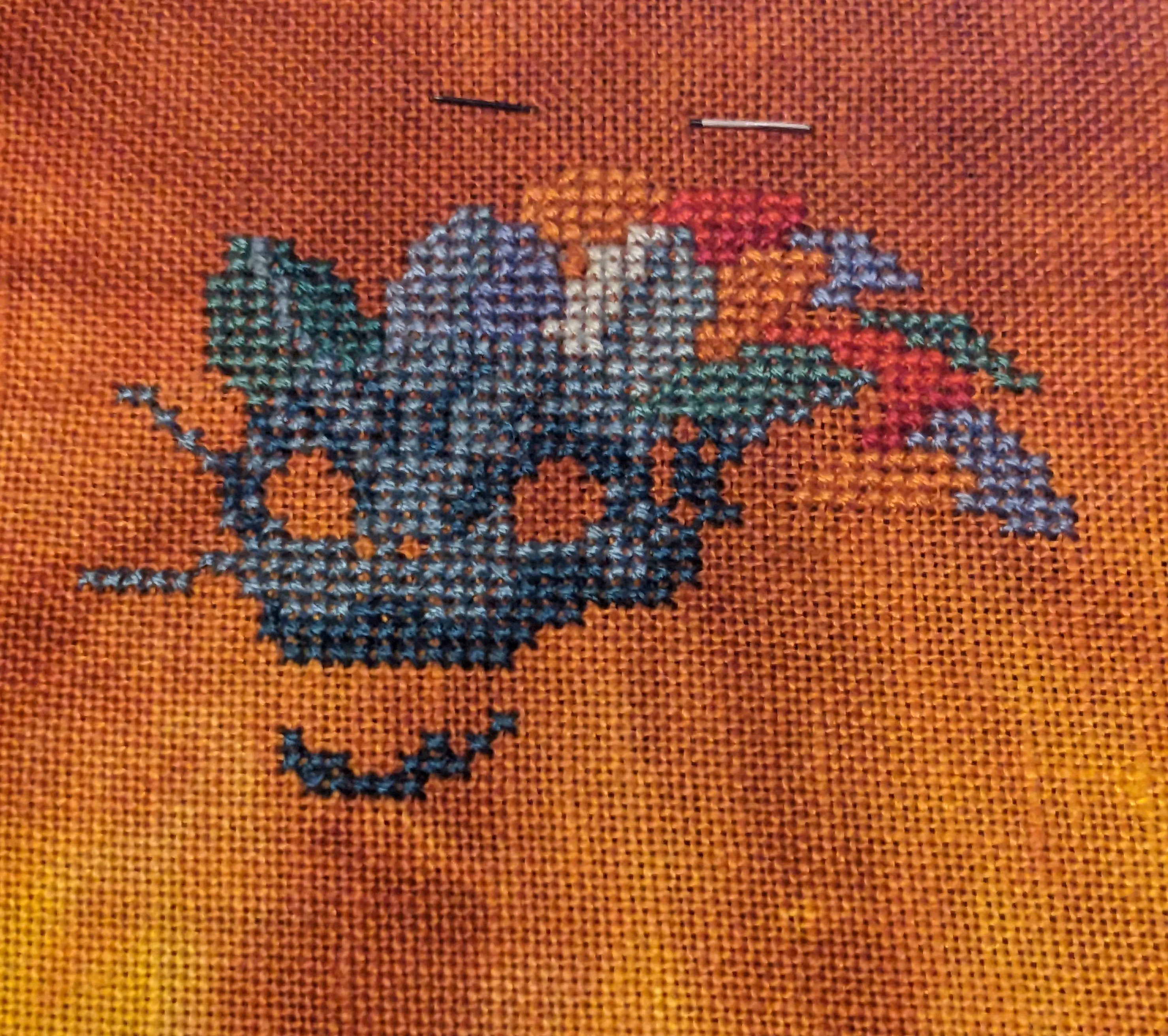 A Cross stitch of a dragon with a blue body and orange mane