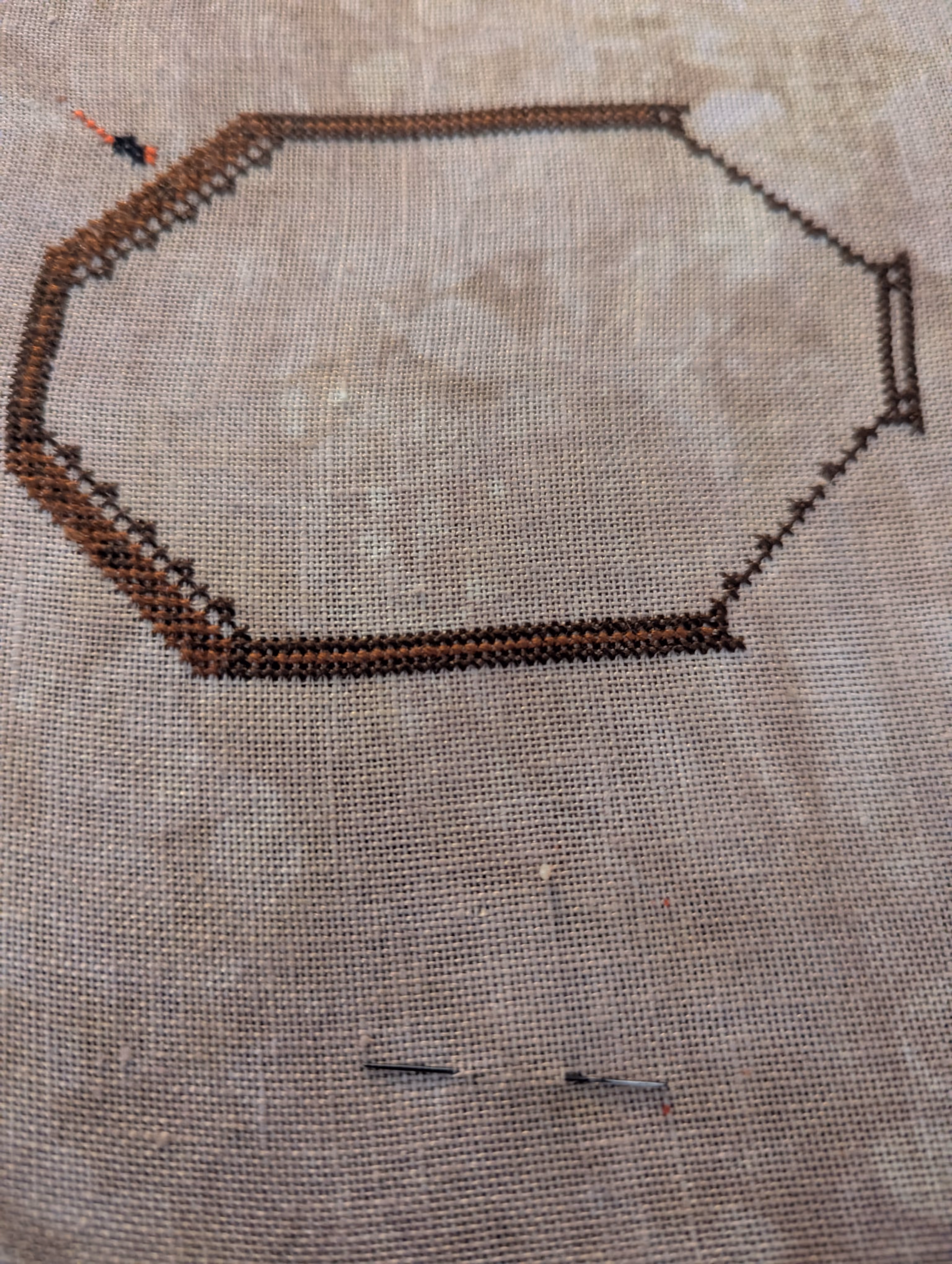The smallest dragon fly next to a frame stitched in shades of brown that will hold a beetle