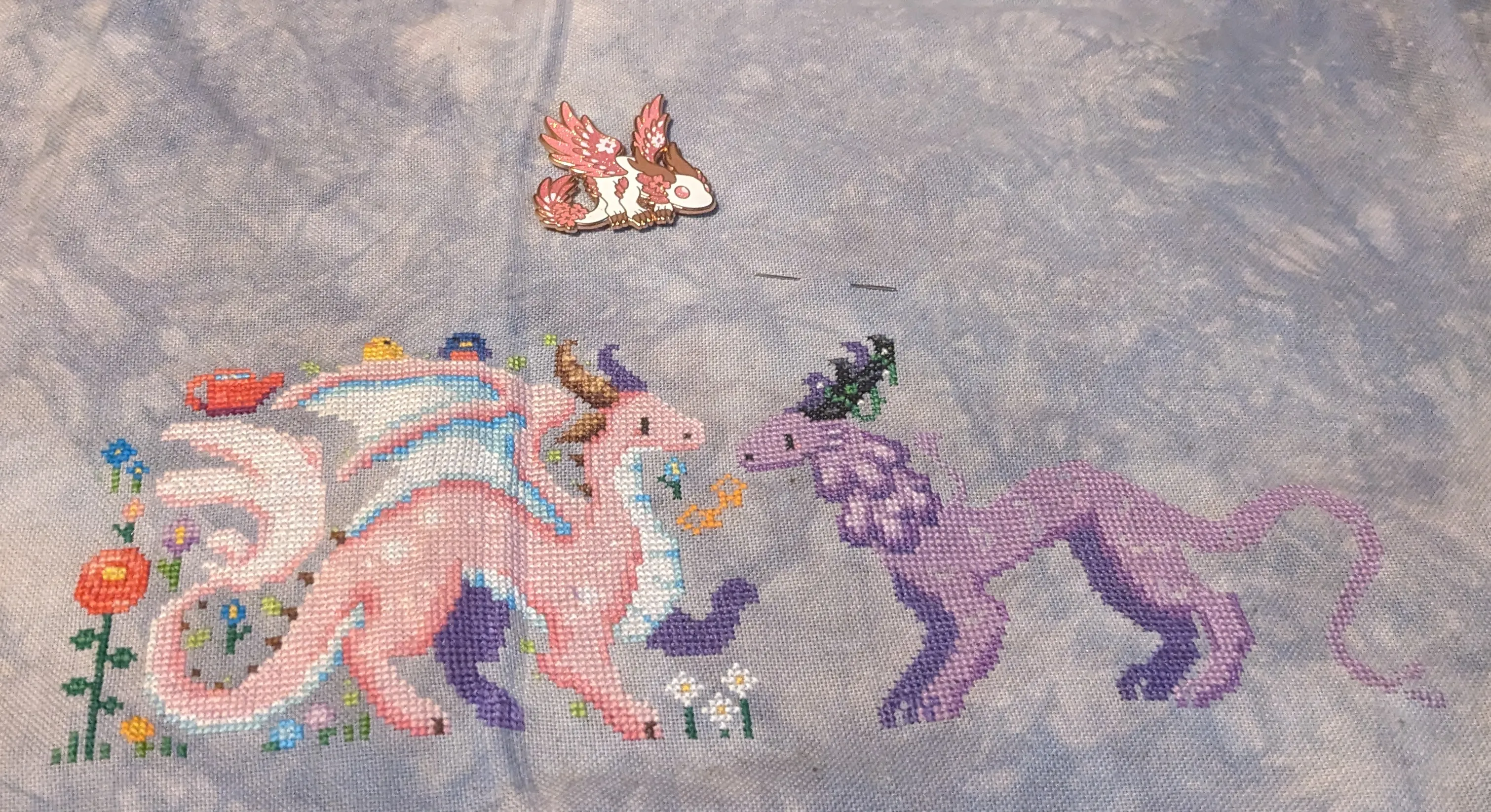 image of two dragons where one is pink with white spots and the other is in shades of purple in a meadow with birds
