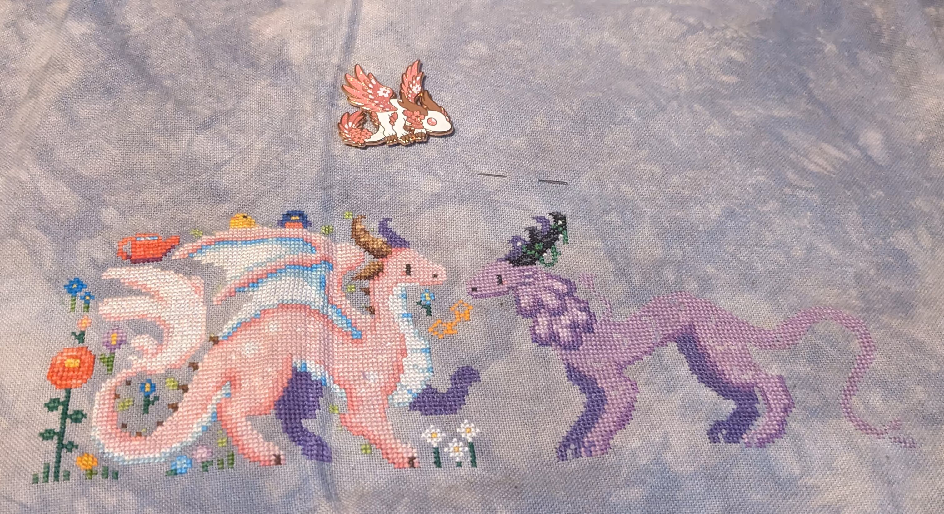image of two dragons where one is pink with white spots and the other is in shades of purple in a meadow with birds