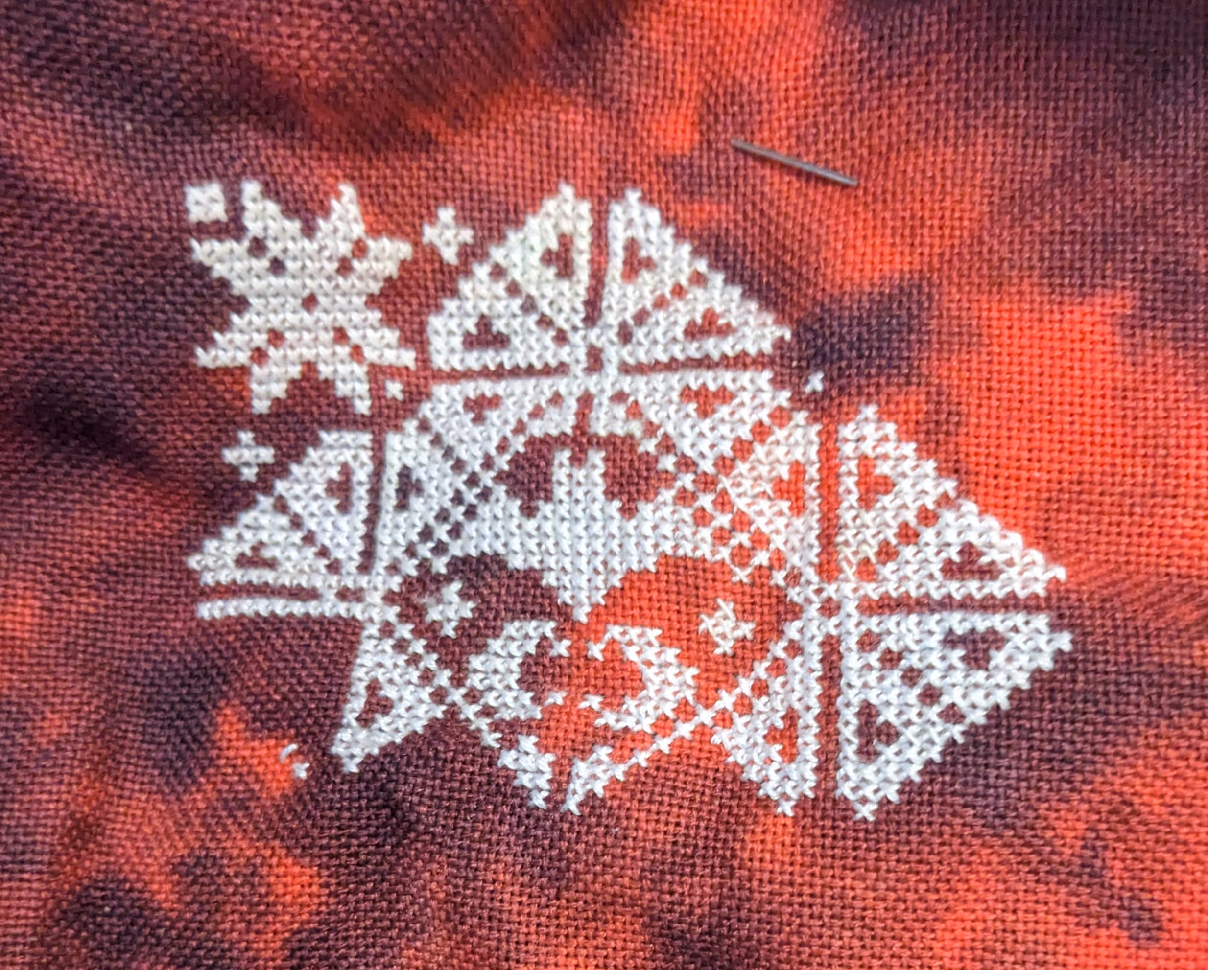 Image of a bat encased in a geometric border in white thread on a red fabric