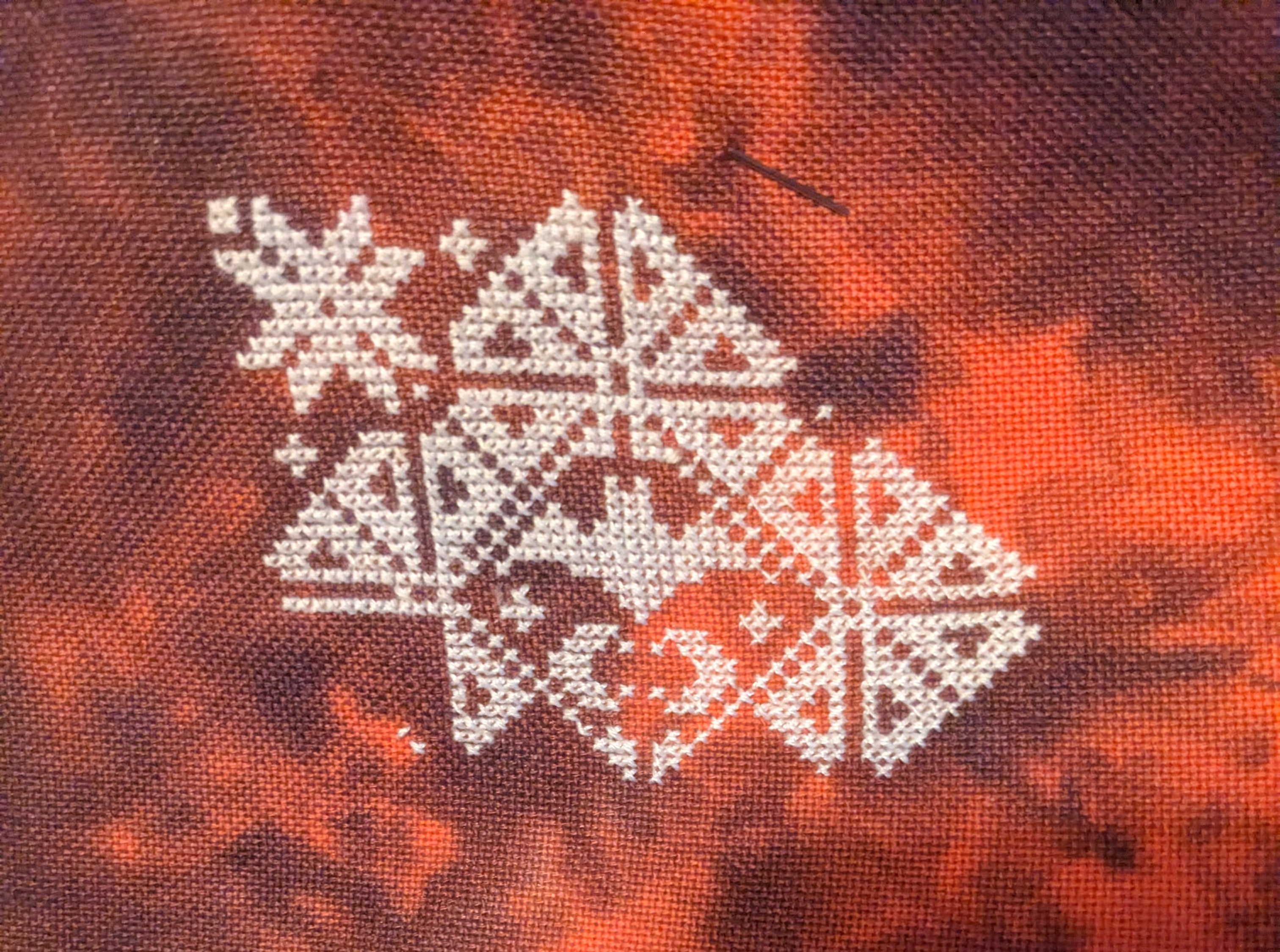 Image of a bat encased in a geometric border in white thread on a red fabric