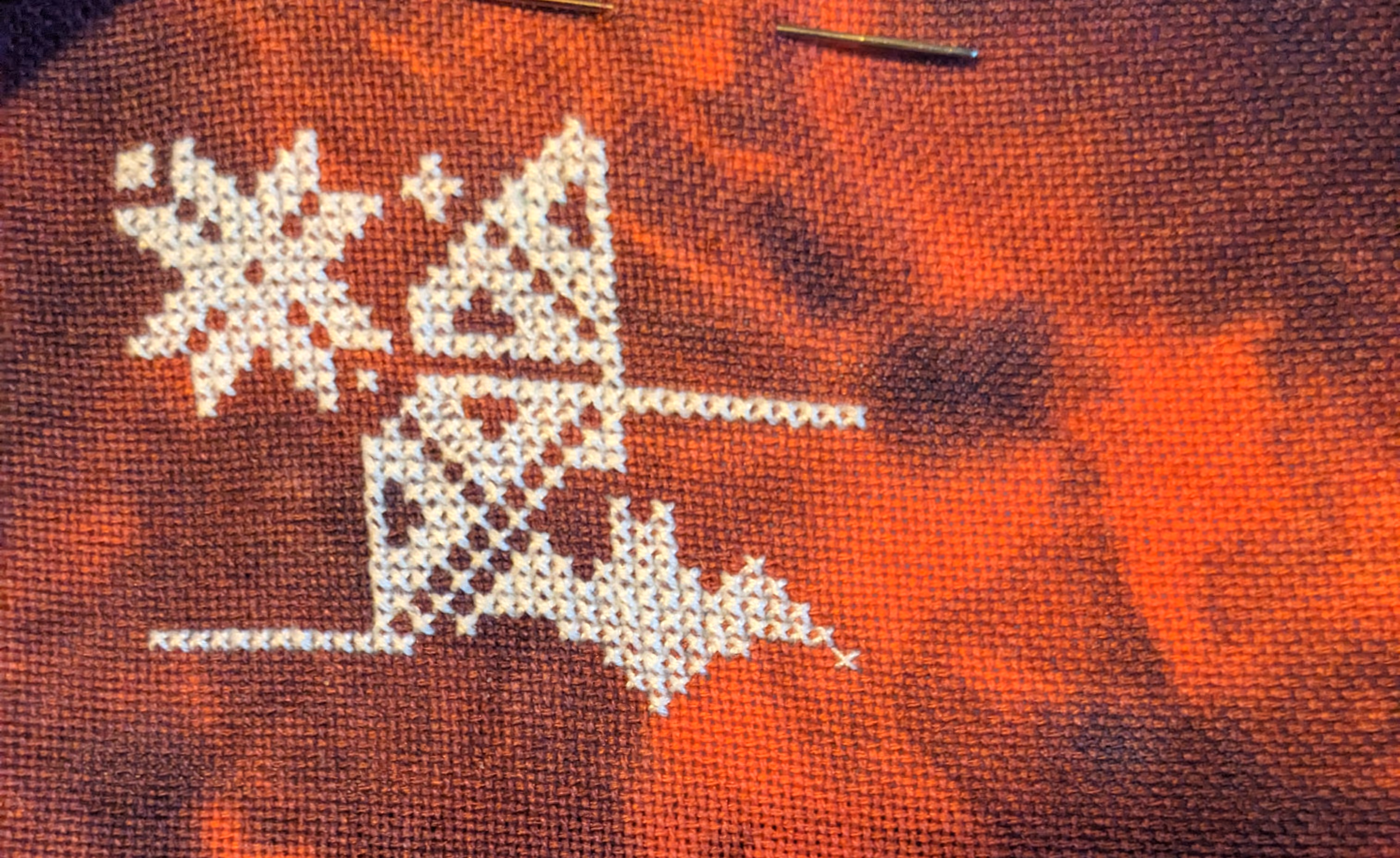 Image of a geometric pattern with a bat in white thread on a gothic red mottled fabric