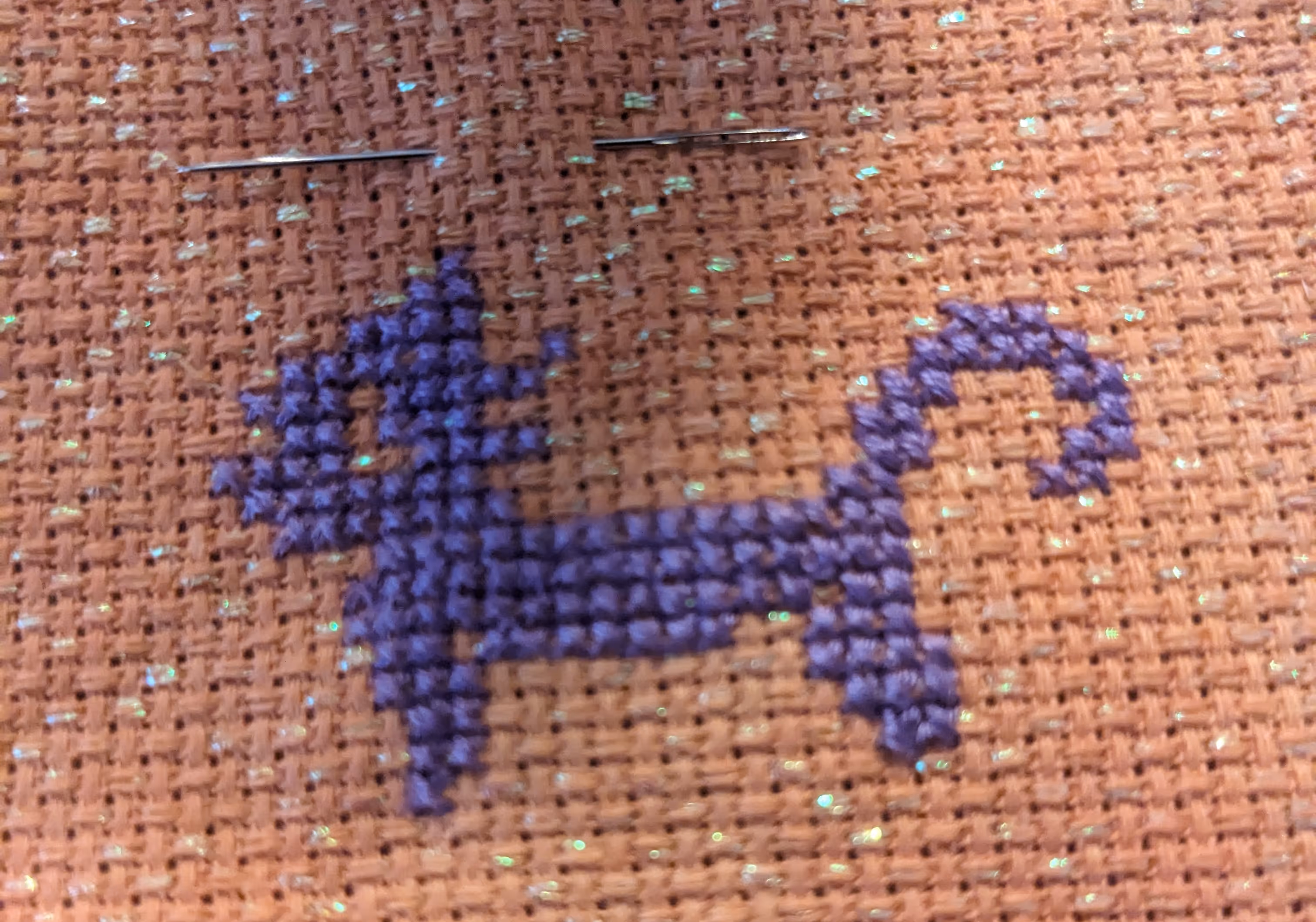 Image of a black cat in cross stitch on an orange opalescent fabric]