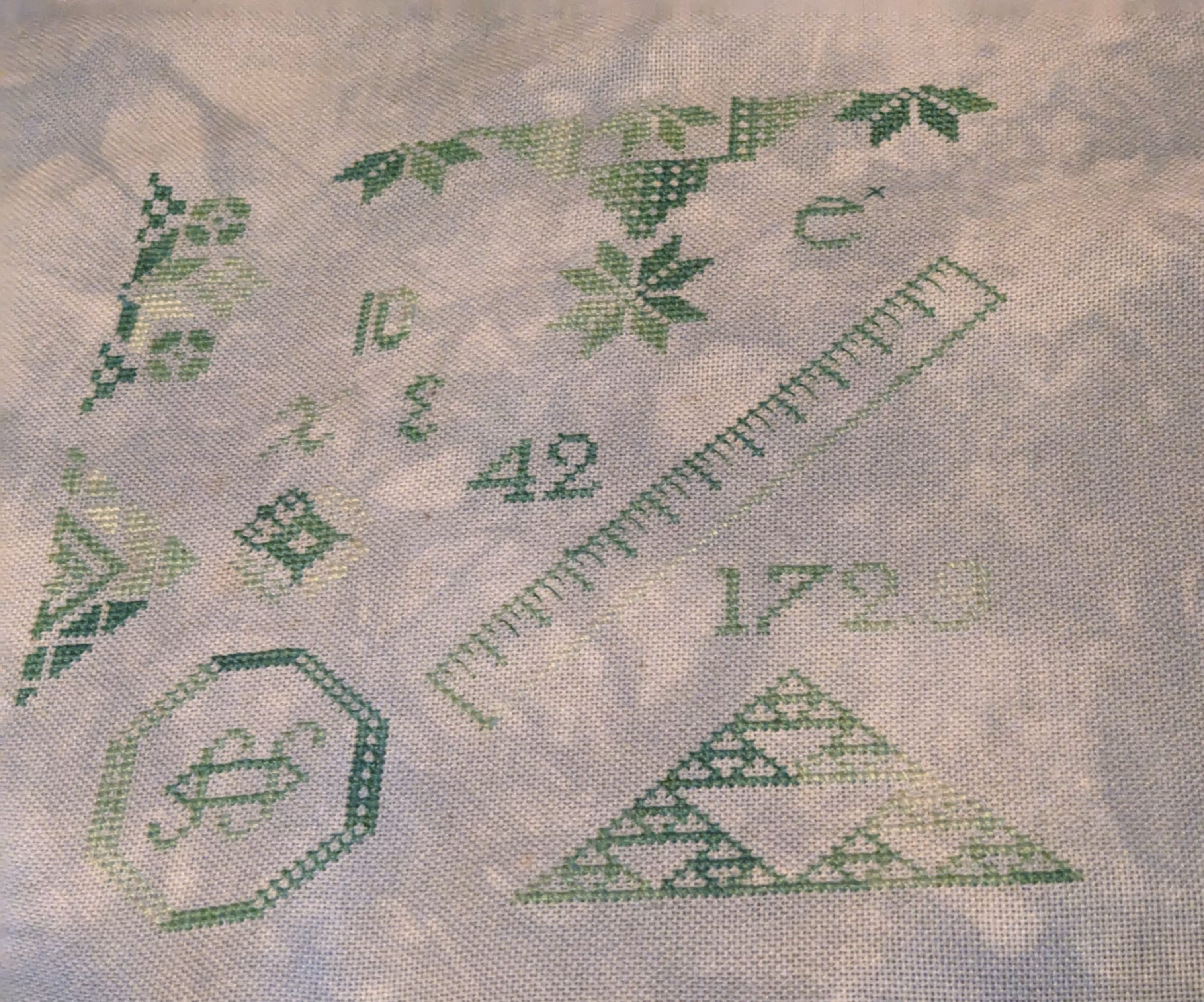 A small cross stitch in the design of a Quaker sampler in shades of green variegated floss with math themed motifs