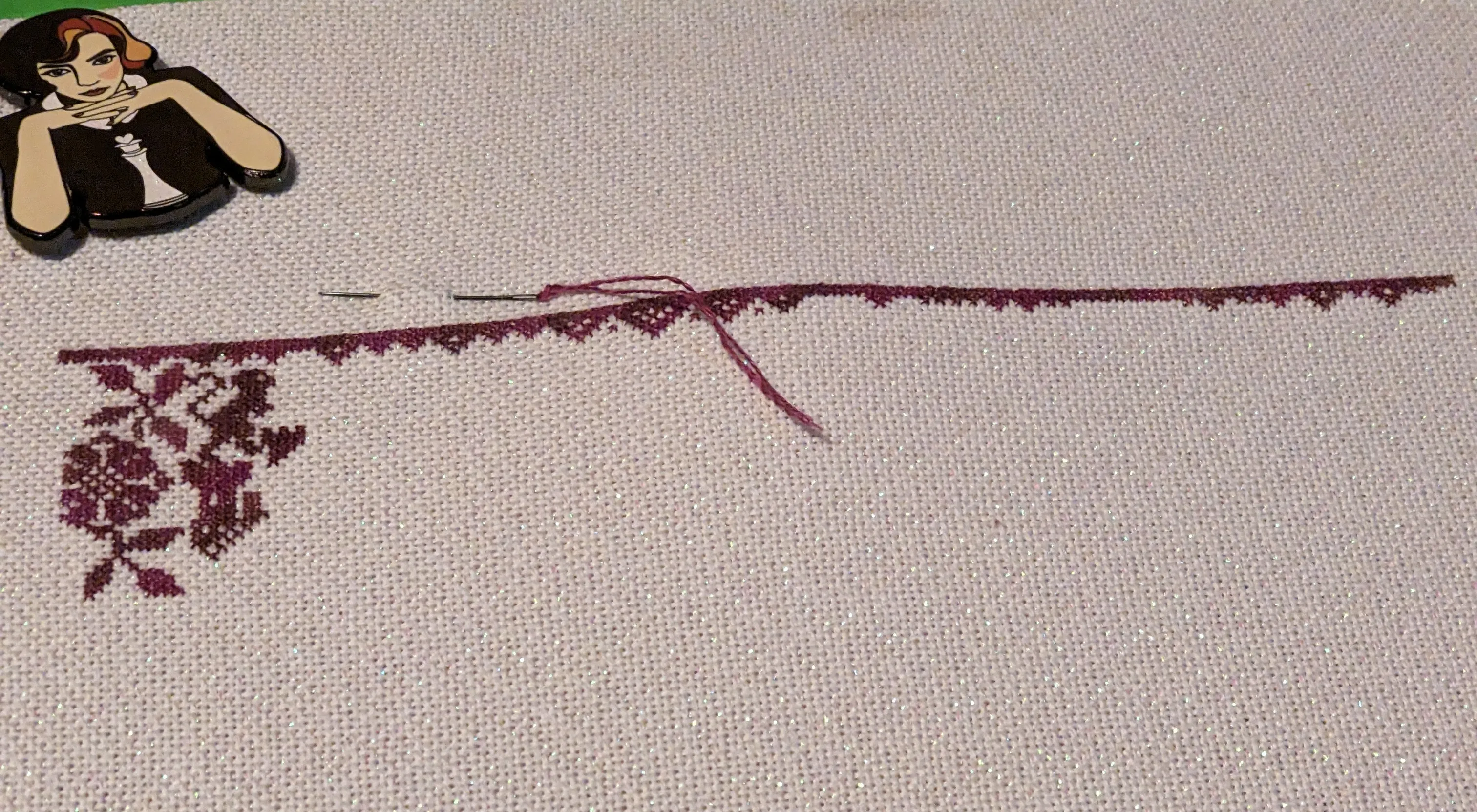 Image of a cross  stitch that shows a border, flower, and a castle