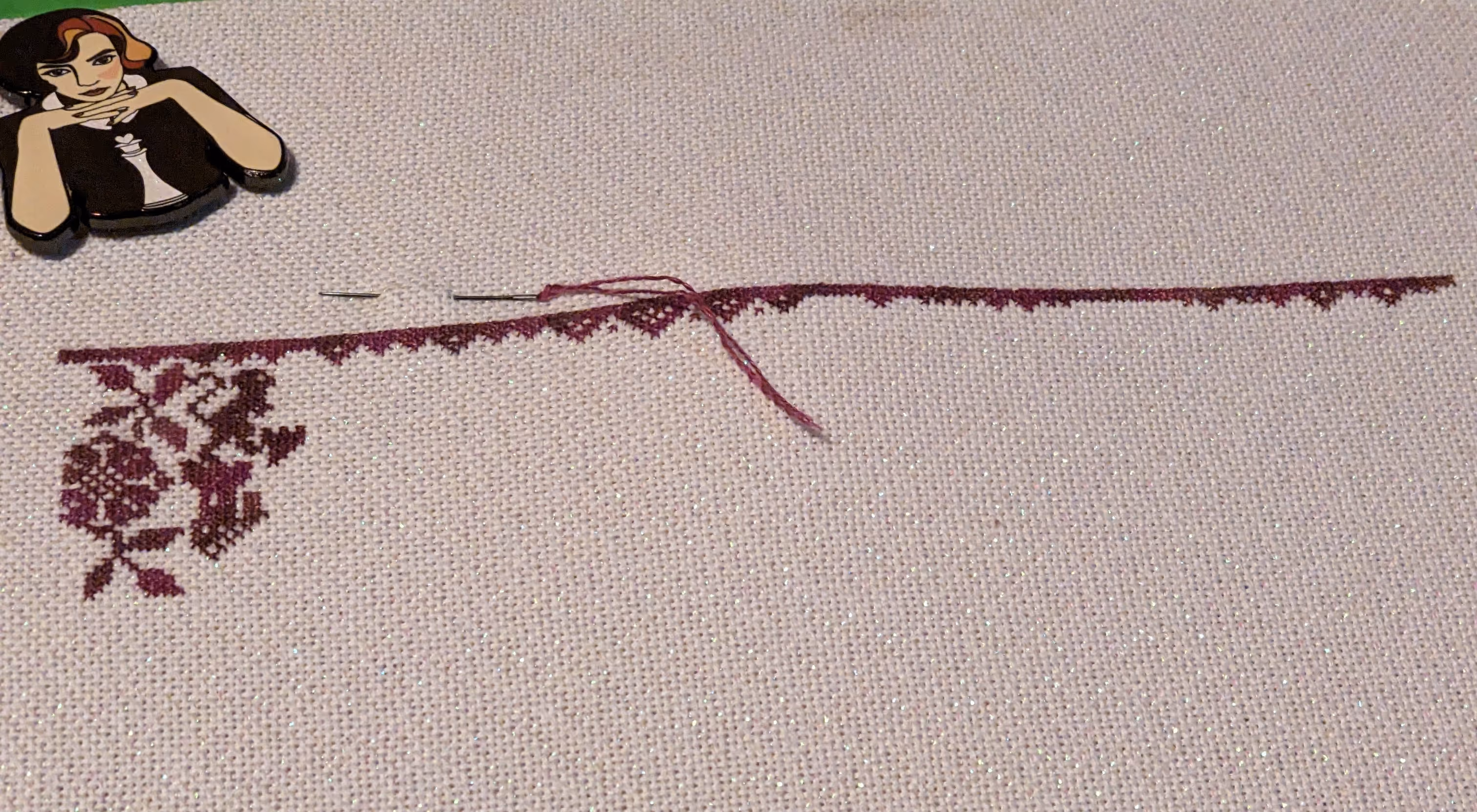 Image of a cross stitch that shows a border, flower, and a castle