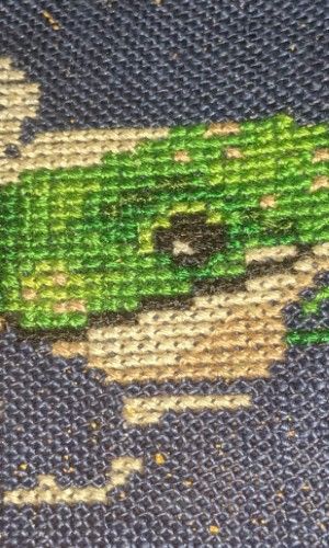 The face of a frog in shades of green rests in this partially stitched tea cup