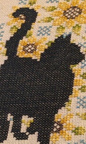 In the foreground is a black cat with a background of sunflowers in the shape of a mandala with metallic threads